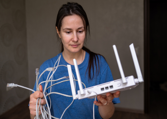 Frustrated woman holding a modem / router with a handful of tangled network cables wishing for better Wi_fi in her home.